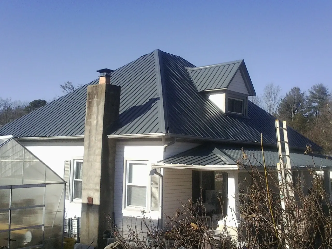 Dark blue standing seam metal roof on a white farmhouse with dormer — Slate & Tile Roof Repair by Roofing Brothers in Rock Spring
