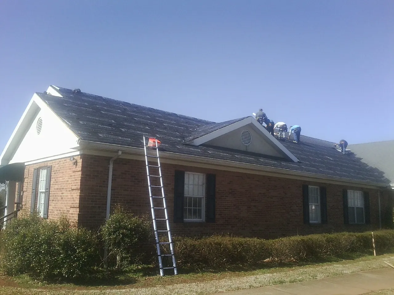 Crew tearing shingles off a brick ranch roof with a ladder set — Emergency Roof Repair work by our crew in Rock Spring