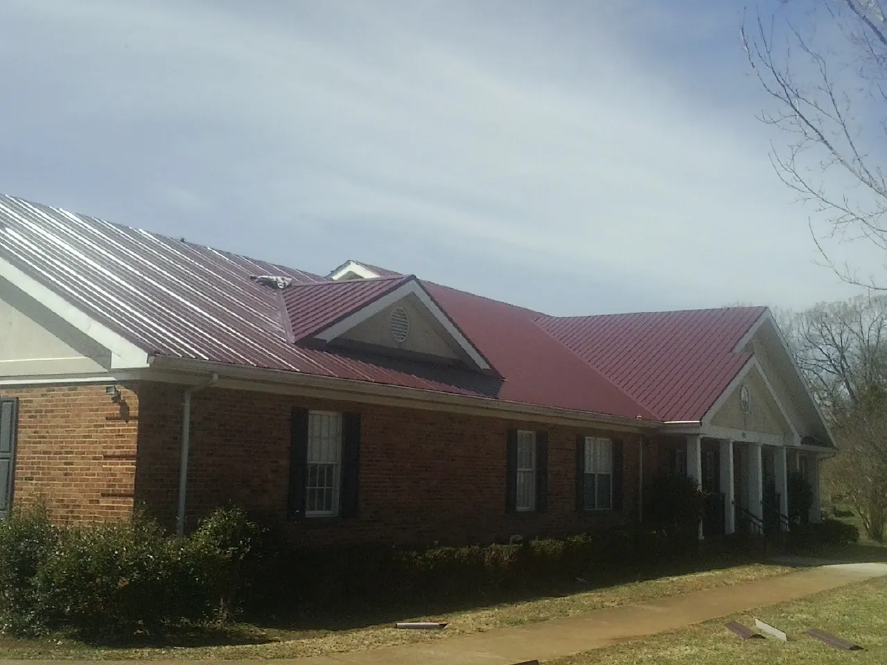 Red metal roof with gabled entries on a long brick building, from a Hail Damage Roof Repair job in Rock Spring