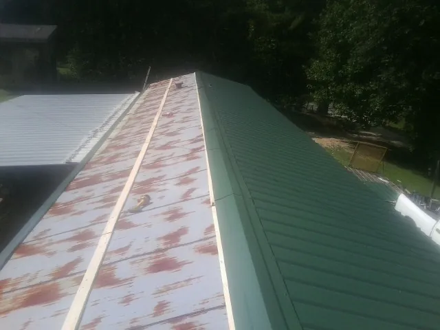 Old rusted panels beside newly installed green metal roofing — Wind Damage Roof Repair by Roofing Brothers in Rock Spring