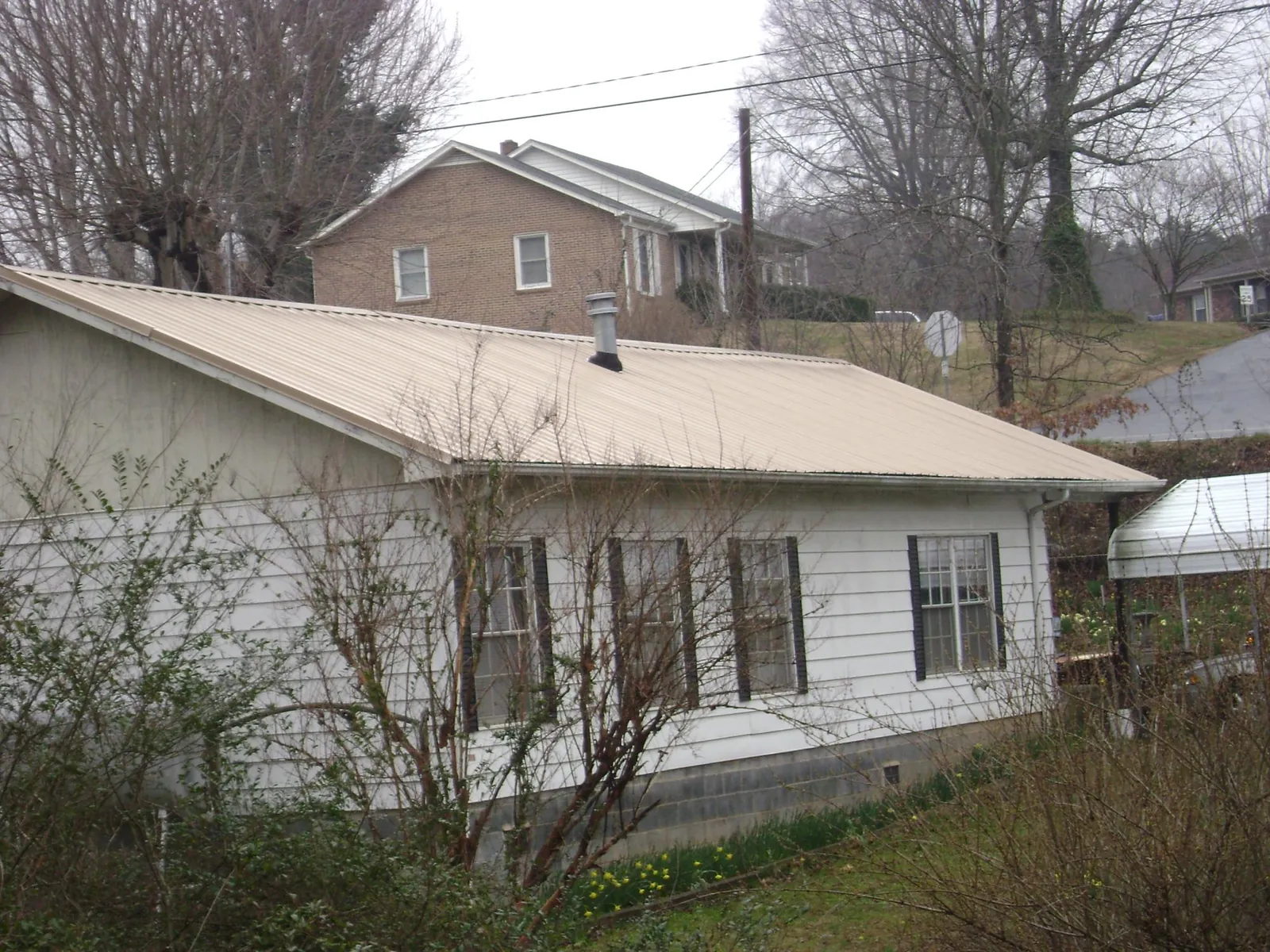 Tan metal roof on a white sided house set into a hillside — Commercial Roofing by Roofing Brothers in Rock Spring